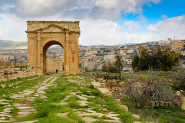 Fototapeta na wymiar Path with Roman gate and cloudy blue sky at Jerash in Jordan