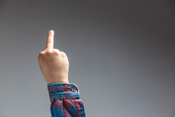 male adult hand showing middle finger insult gesture in studio shot isolated on grey background