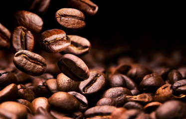Coffee beans falling on pile, black background with copy space, close up