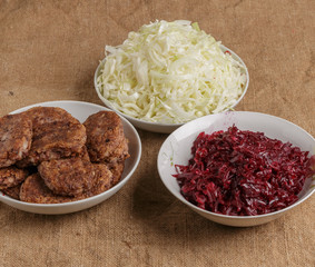 Fresh cutlets, beets and cabbage on plates.