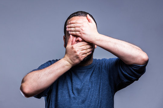 Young man wearing blue shirt Covering eyes and mouth with hands, surprised and shocked. Hiding emotion