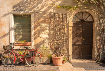 Fototapeta na wymiar Exterior of ann old, abandoned house with a red bicycle and potted plants in a street of the medieval town of Lazise on Lake Garda, Veneto, Italy