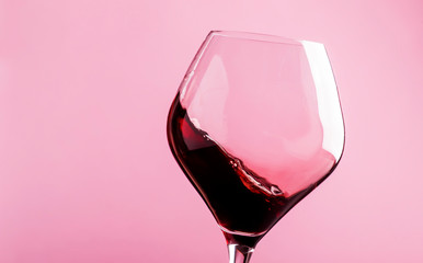 Dry red wine, splash in glass, pink background, defocused in motion image, shallow depth of field
