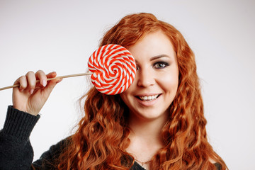 Beautiful young redhead woman holding a red white lollipop on white background