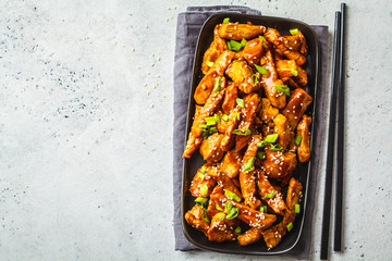 Teriyaki chicken with sesame, green onion in black plate, top view.