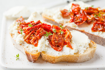 Ricotta and sun dried tomatoes sandwiches on white board.