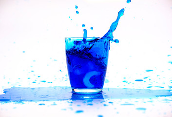 Blue water splashing in glass on white background