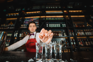 Professional male bartender serving the order, pouring alcoholic drink in a row of shot frozen glasses in a night club