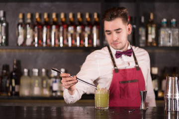 Bartender finishes decoration of his cocktail with ice cubes and lime slice using tweezers