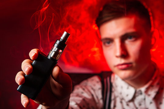 A man shows an electronic hookah. A man in the smoke from cigarettes. Steam from vape. Electronic Cigarette. A man with vape. Vaper.