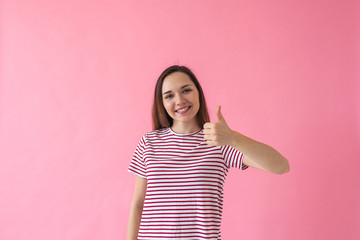 Positive smiling girl on a pink background shows fingers gesture meaning Like or Ok.