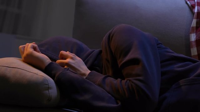 Young male sleeping in cheap hostel, hiding in hood from light and noise, teen