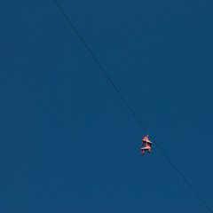 Orange roller skates hanging on a wire against blue, clear sky. Minimalistic. Square format. Contrasting colors.