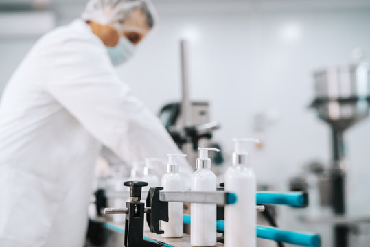 Picture of bottles with hair conditioner in row on exit of pouring machine. Chemical factory interior. In background chemist.