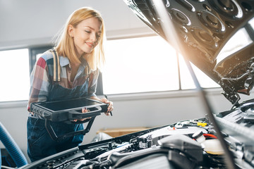 happy fair-haired girl is working with a car diagnostic system recognizing a failure condition,...