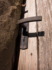 Ein Gartentor bei Sonnenschein aus Holz mit Holzbretter und einem Türgriff auch Türklinke genannt, aus Metall.