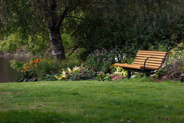 Naklejka premium Yellow wooden bench in a park with flowers in the background