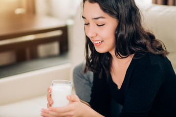Beautiful young woman with glass of milk at home