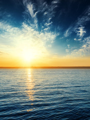 orange sunset in dark blue sky with clouds over river