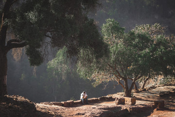 Young man sitting on a wall under a tree close to the Church of St. George (Bete Giyorgis) in Ethiopia during sunset