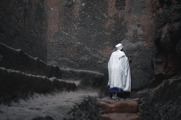 Old priest in white robe praying at a wall at the lalibela church in ethiopia 