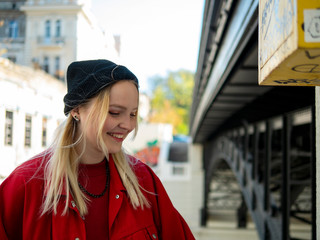 portrait of a smiling young attractive girl in a red jacket and knitted black jacket under the bridge