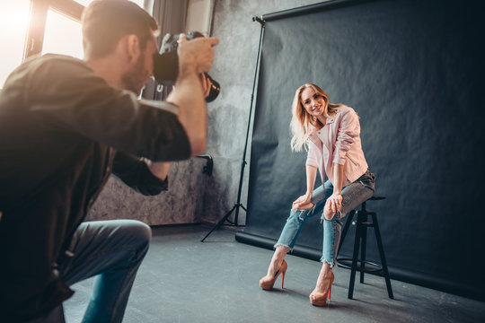 smiling positive model in fashion clothes sitting on the chair and posing to the photographer