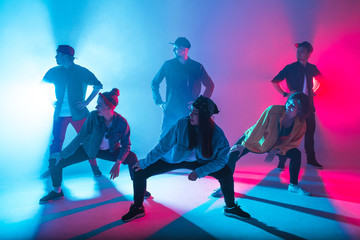 Group of diverse young hip-hop dancers in studio with special lighting effects in blue and pink...