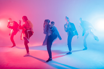 Group of diverse young hip-hop dancers in studio with special lighting effects in blue and pink...