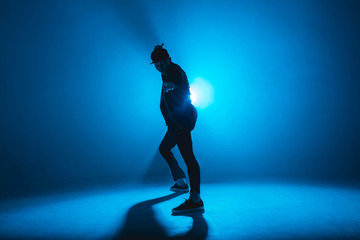 Fototapeta na wymiar Full-size of silhouette of male break dancer performing on blue neon stage his expressive dance, Dark blue background with light flare on background
