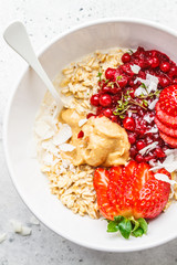 Oatmeal porridge with berries, peanut butter and coconut in white bowl. Healthy vegan food concept.