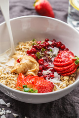 Oatmeal porridge with berries, peanut butter and coconut in white bowl, dark background. Healthy vegan food concept.