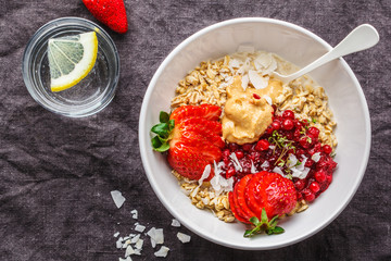 Oatmeal porridge with berries, peanut butter and coconut in white bowl, dark background. Healthy vegan food concept.