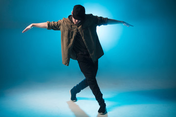 A dark silhouette of a singer on the stage, dancing alone during performance on dark blue neon background with smoke and lights.