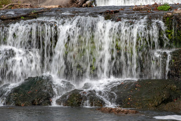 Fototapeta premium Water flows in a vertical drop creating a beautiful waterfall that spashes on the smooth boulders.