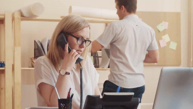 an employee of the call center is talking on the phone and writing a text on paper, a colleague passes by, gives her five and goes to look for the folder.
