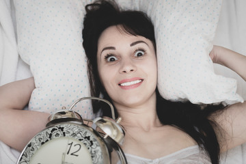the young woman woke up in the morning from the alarm clock and in a panic looks surprised . The...