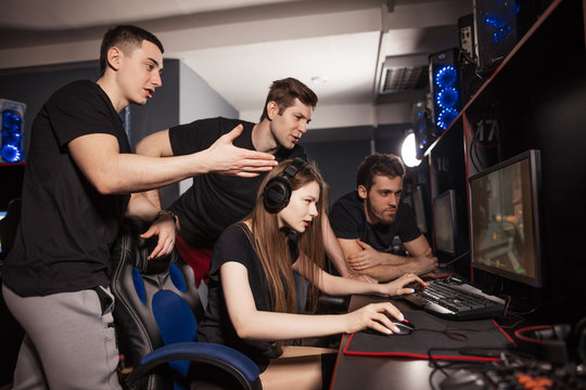 Young woman playing computer game in club and her friends supporting her and cheering, standing behind. Cyber sport, E-sport, Friendship concept