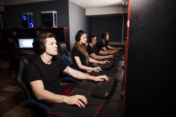 Obraz premium Young female and male gamers playing video game while spending weekend leisuretime at pc gaming club, focused serious people behind pc monitor at dark room. Entertainment or addiction concept