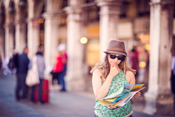 Beautiful tourist woman is confused about finding directions. She is holding a map and hand on the chin.