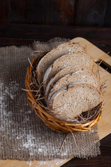Fototapeta na wymiar Freshly sliced pieces in a wicker bowl on an oak board with scattered flour on a wooden background with of linen fabric. Photo top view. Vertical photo