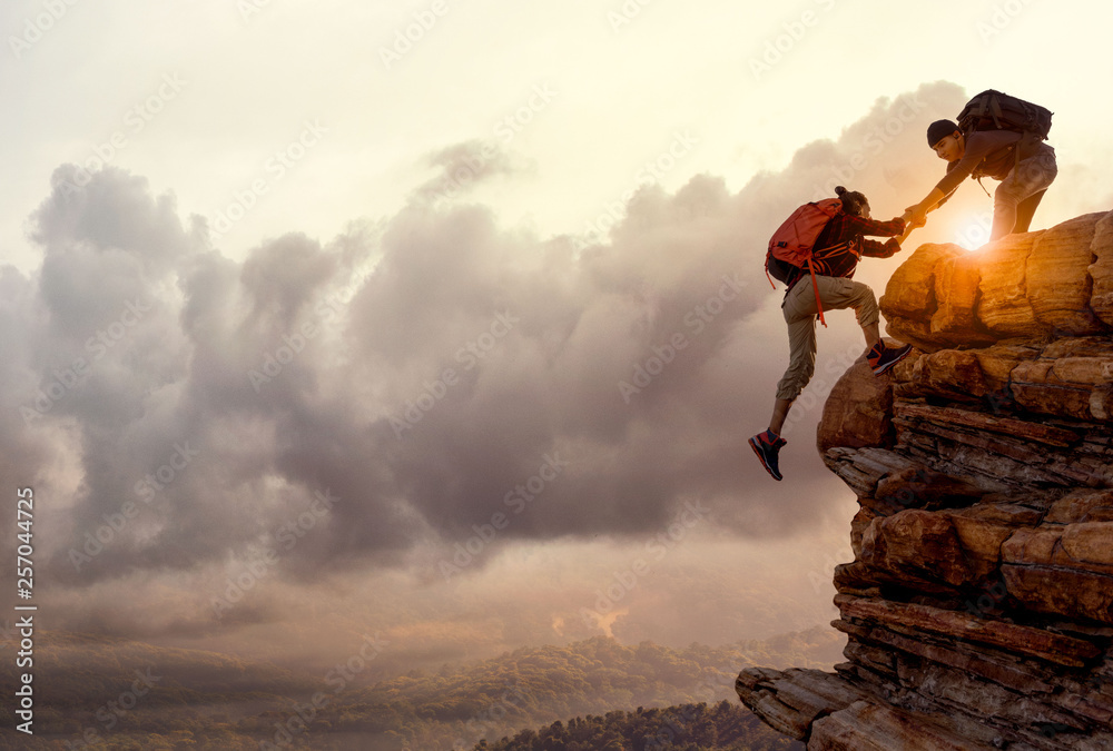 Wall mural people helping each other hike up a mountain at sunrise. giving a helping hand, and active fit lifes