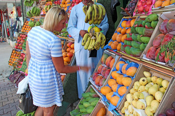 Woman choosing fruits in tray from street vendor. Girl buying mangoes