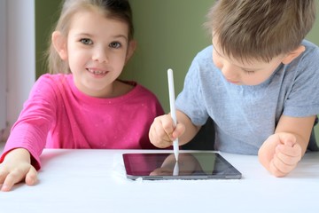 White caucasian toddler boy and beautiful girl drawing together on tablet screen. Portrait of a happiness little brother and sister. Children play a computer game on the tablet