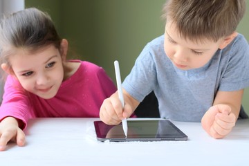 White caucasian toddler boy and beautiful girl drawing together on tablet screen. Portrait of a happiness little brother and sister. Children play a computer game on the tablet