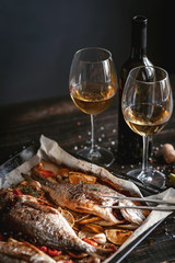 dinner concept for two. two glasses of white wine, baked fish.
