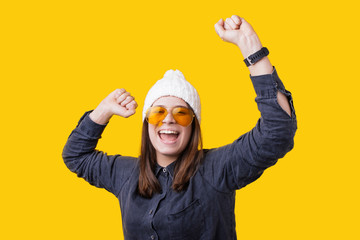 Portrait of happy cute young woman with toothy smile raised hands and celebrate achievement goal. Isolated over yellow background