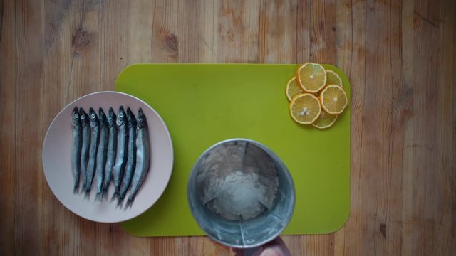 Top view of a male hands sprinkling flour through a sieve onto a green chopping board, he prepares a place to cover the capelin with breading.