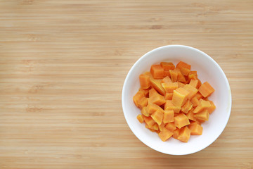 Boil chopped sweet potatoes in white bowl against wooden board background with copy space.