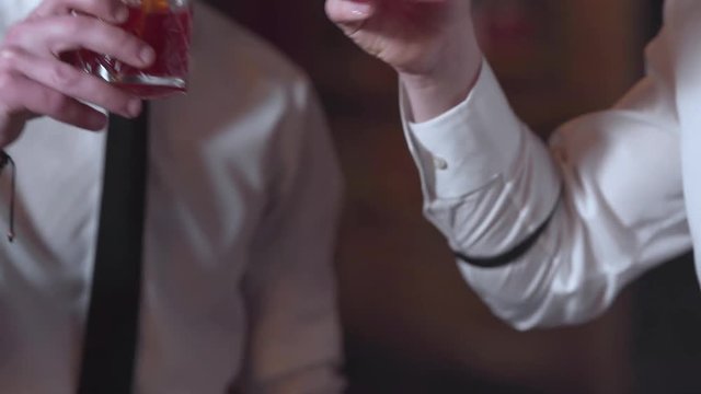 Hands Of Bartenders With Red Cocktails in Glasses With Orange Slices Chears Up and Drink It. Blurred Background